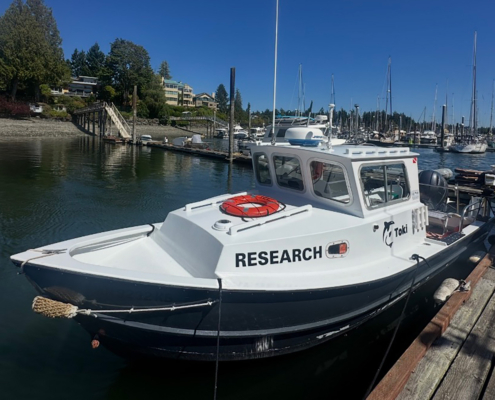 White research boat moored at a marina, with 'RESEARCH' on its hull and calm water nearby.