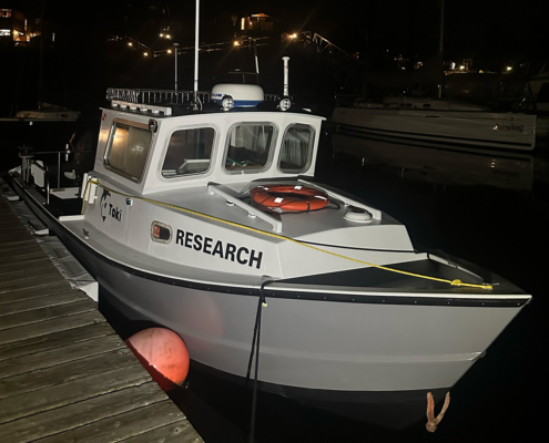 White research boat moored to a wooden dock at night, with an orange life ring on deck and 'RESEARCH' on the hull.
