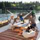 1EEE6E71-CC4A-407B-885F-38EC594442EF | Sail Bainbridge | Captained Sailing Adventures | Bainbridge Island | Seattle Family of four with a dog relaxing on a boat deck around a wooden table with flowers by a lake.
