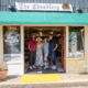 Four people stand in the open doorway of a marine-supplies shop named The Chandlery, with a green awning and a yellow table outside.